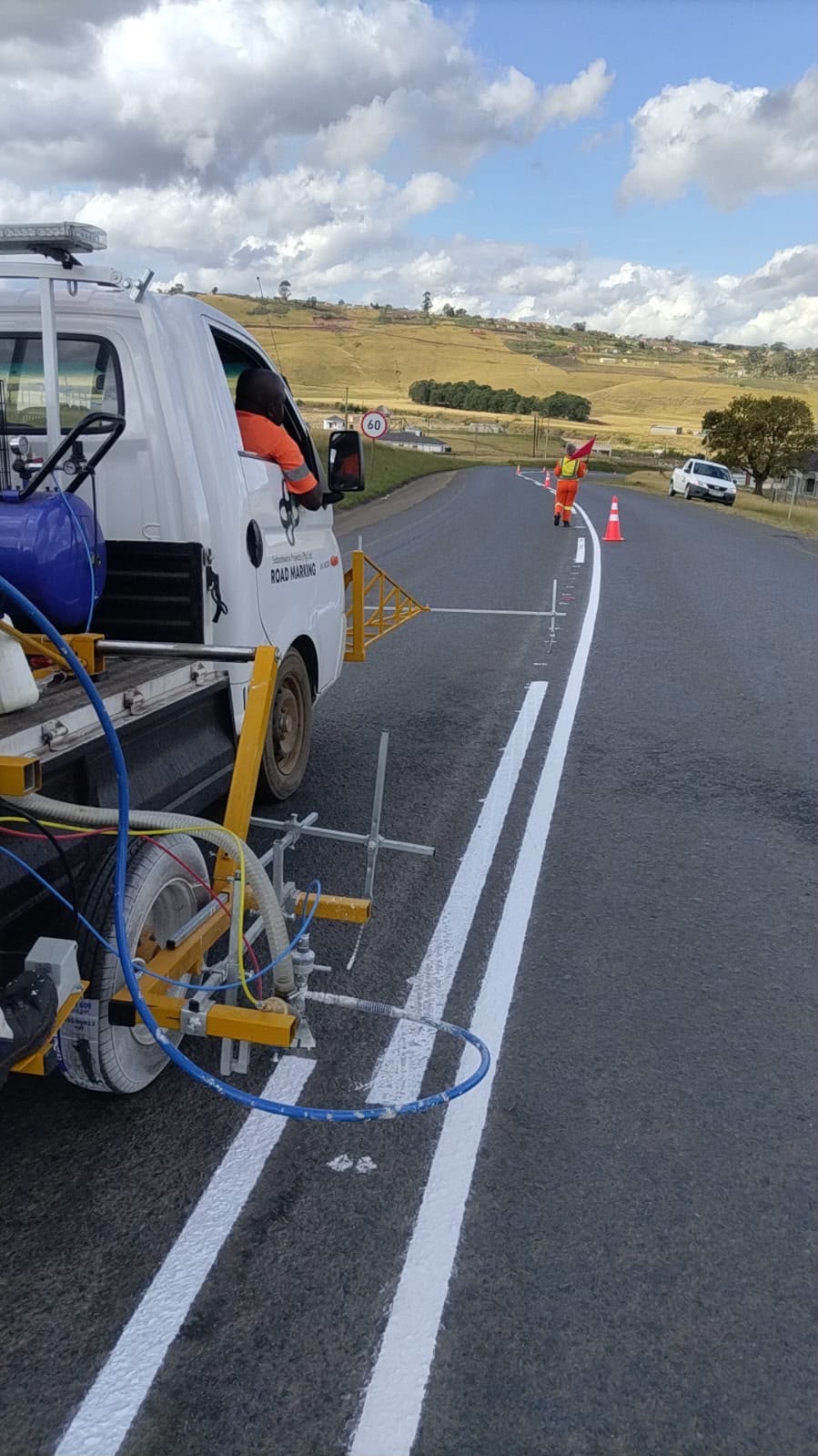 Sobantwana Projects line-marking truck applying double centre lines with crew flagger ahead