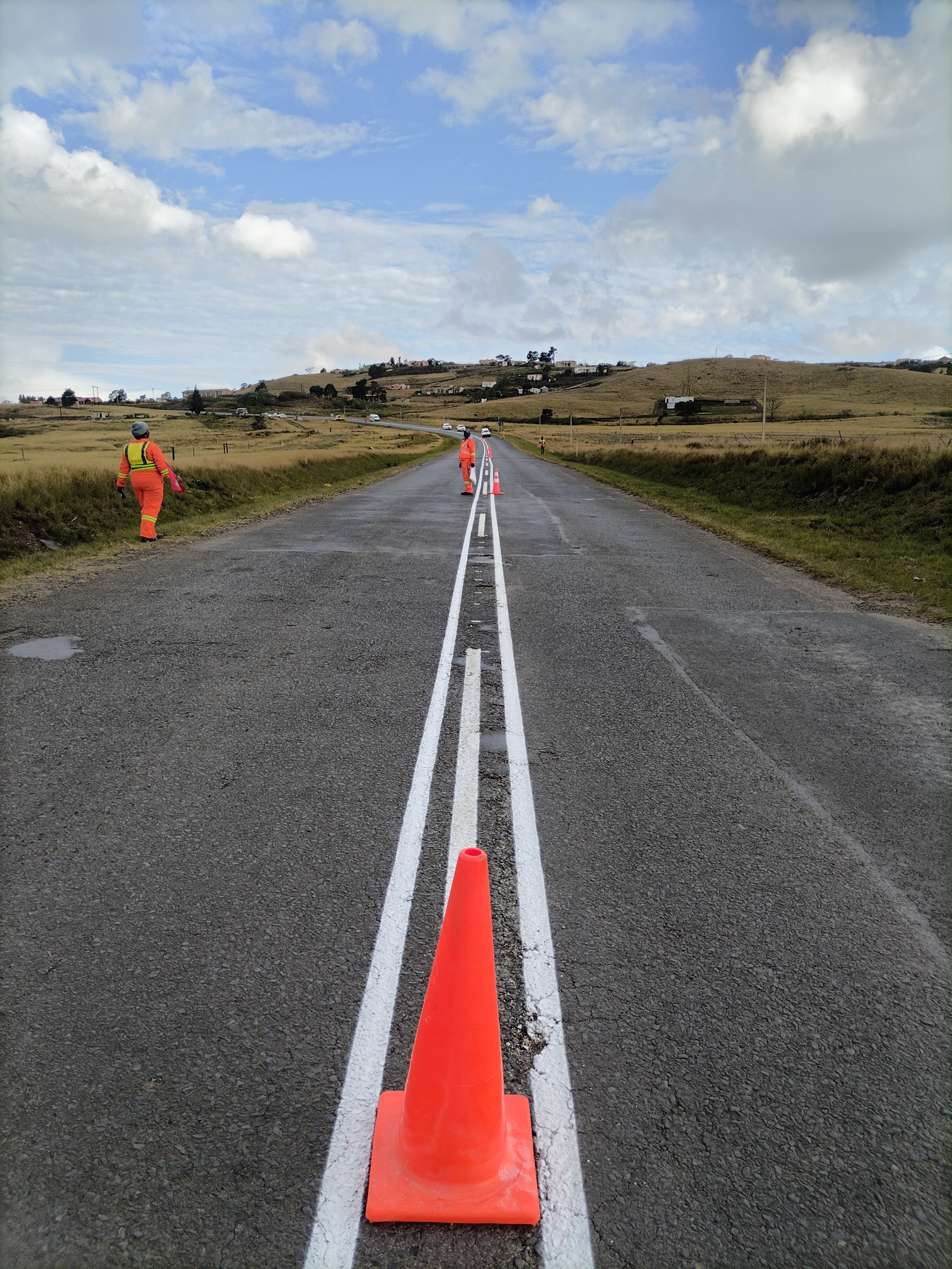 Freshly painted double centre lines on a rural road with traffic cone and Sobantwana Projects crew
